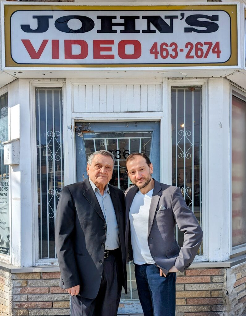 John and Frank standing in front of John's Video Store on Pape Avenue in Toronto, Ontario